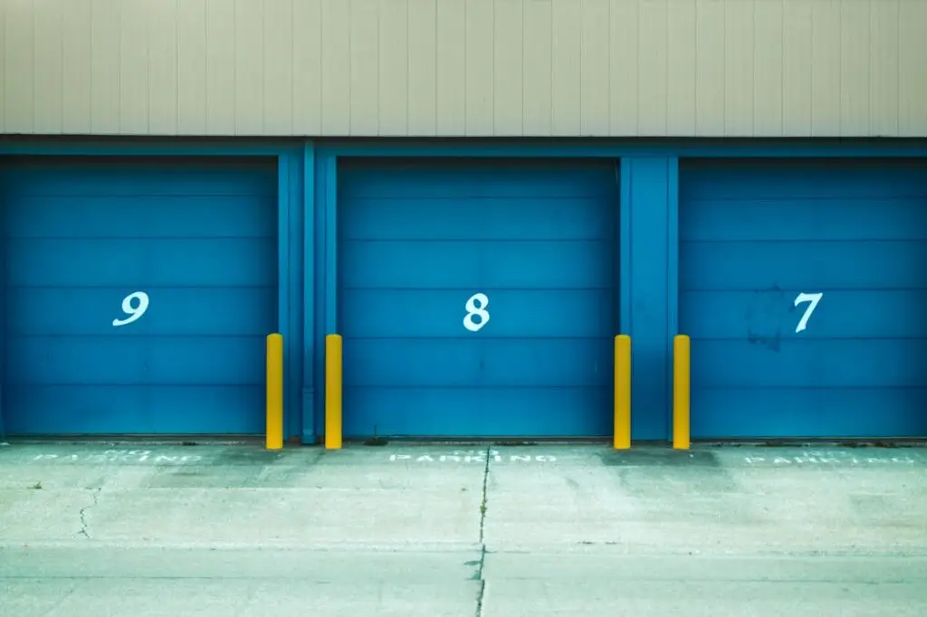 Three blue shutter doors numbered 9, 8, and 7 with yellow barriers in urban environment.